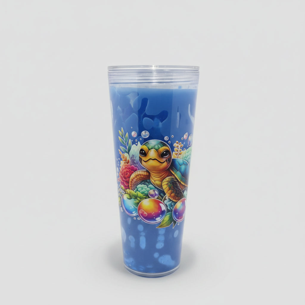 A tall clear plastic tumbler with a blue interior, featuring a colorful underwater graphic of a sea turtle, coral, and bubbles, set against a gray ribbed background.